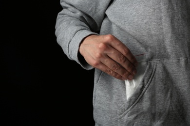Drug dealer taking bag with cocaine out of pocket on black background, closeup. Space for text