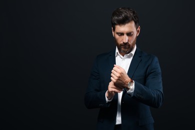 Handsome bearded man adjusting cufflinks on black background. Space for text