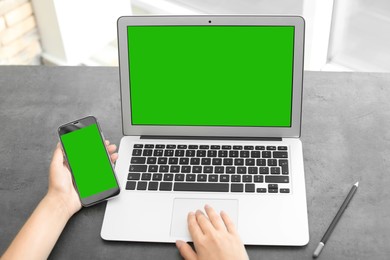 Image of Woman using laptop and smartphone at desk, closeup. Devices displays with chroma key