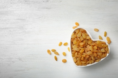 Bowl of raisins on wooden background, top view with space for text. Dried fruit as healthy snack