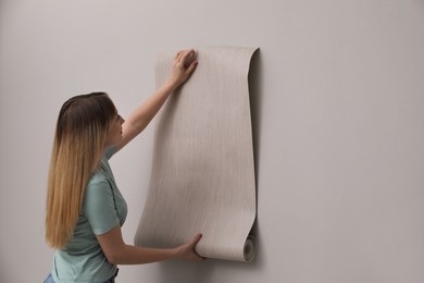 Woman hanging stylish wall paper sheet indoors