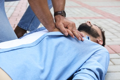 Passerby performing CPR on unconscious young man outdoors, closeup. First aid