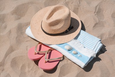 Straw hat, beach towel, seashells and flip flops on sand