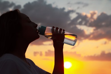 Young woman drinking water to prevent heat stroke outdoors at sunset