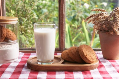 Glass of milk with cookies on red checkered tablecloth indoors
