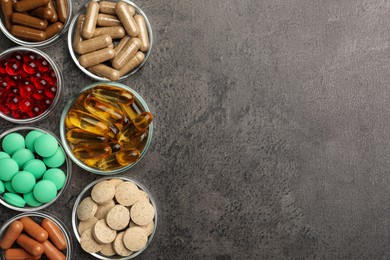 Different dietary supplements in glass bowls on grey table, flat lay. Space for text