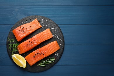 Photo of Fresh raw salmon, slice of lemon and spices on blue wooden table, top view. Space for text