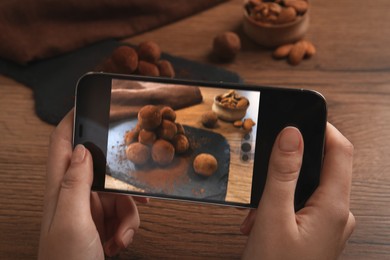 Woman taking photo of tasty chocolate truffles served on wooden table, closeup