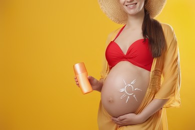 Young pregnant woman with sun protection spray on yellow background, closeup. Space for text
