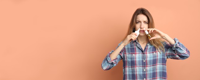 Sick young woman using nasal sprays on coral background