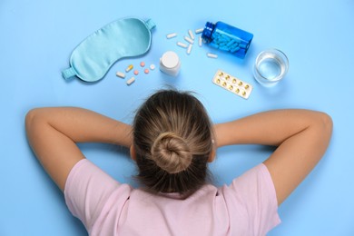 Woman surrounded by different pills on turquoise background, top view. Insomnia treatment