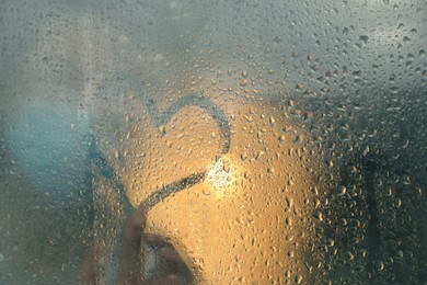 Photo of Woman drawing heart on foggy window at rainy weather, closeup