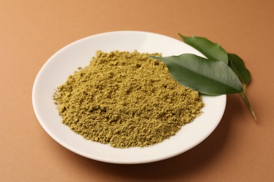 Photo of Henna powder and green leaves on coral background. Natural hair coloring