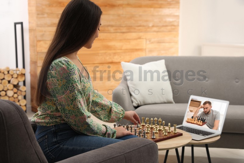 Young woman playing chess with partner via online video chat in living room