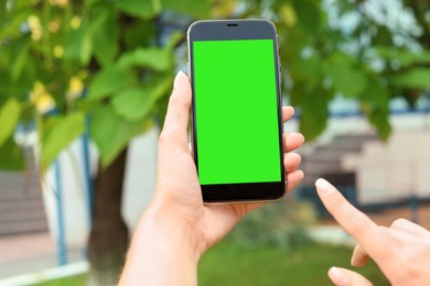 Image of Woman using smartphone with green screen outdoors, closeup. Gadget display with chroma key. Mockup for design