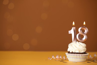 Coming of age party - 18th birthday. Delicious cupcake with number shaped candles on orange background, space for text