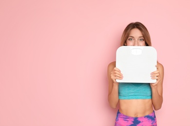 Surprised slim woman satisfied with her diet results holding bathroom scales on color background
