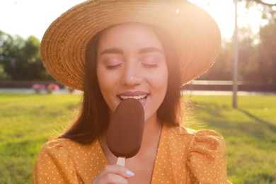 Beautiful young woman eating ice cream glazed in chocolate outdoors, closeup