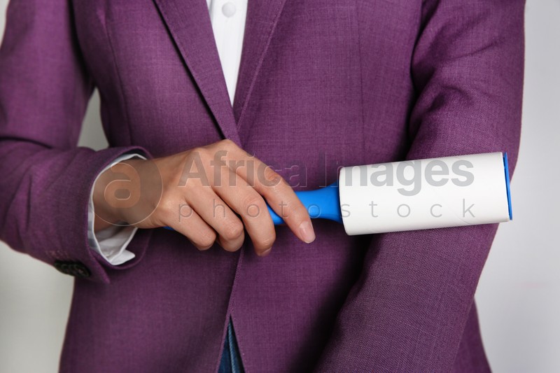 Photo of Woman cleaning purple jacket with lint roller on light grey background, closeup