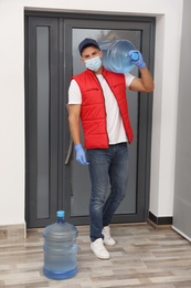 Courier in face mask with bottles of cooler water in entryway. Delivery during coronavirus quarantine