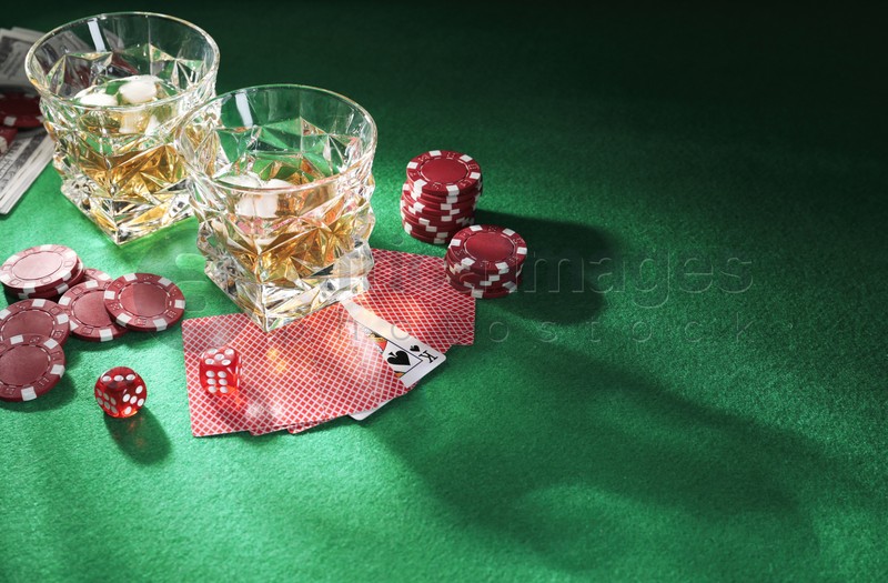 Casino chips, dice, playing cards and glasses of whiskey on green table, space for text