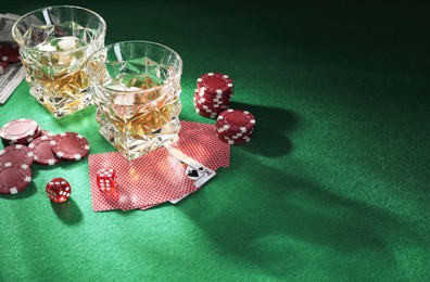 Casino chips, dice, playing cards and glasses of whiskey on green table, space for text