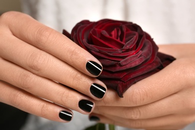 Woman with black manicure holding rose, closeup. Nail polish trends