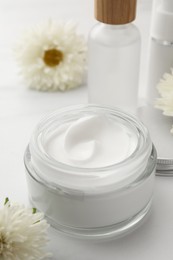 Glass jar of face cream, different cosmetic products and flowers on white marble table