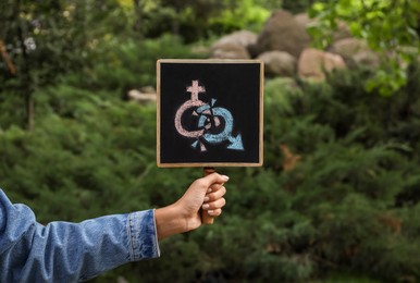 Woman holding chalkboard with gender symbols outdoors, closeup