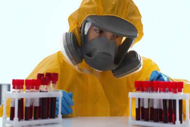 Scientist in chemical protective suit working with blood samples on white background. Virus research