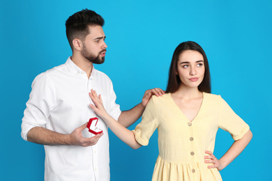 Young woman rejecting engagement ring from boyfriend on blue background