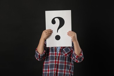 Child holding sheet of paper with question mark on black background