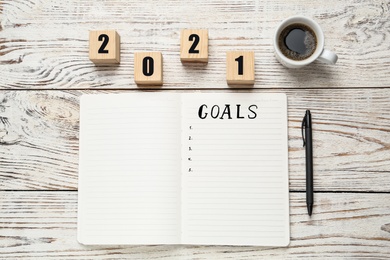 Notebook with word Goals near number 2021 made of cubes, new year aims. Objects on white wooden table, flat lay
