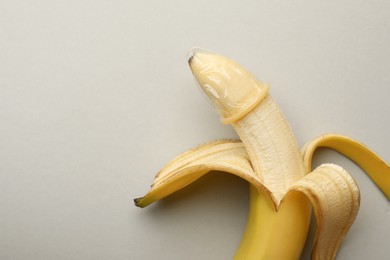 Banana with condom on light grey background, top view and space for text. Safe sex