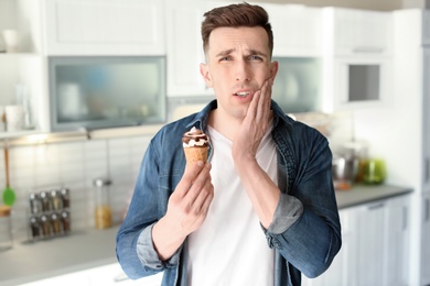 Young man with sensitive teeth and cold ice cream in kitchen