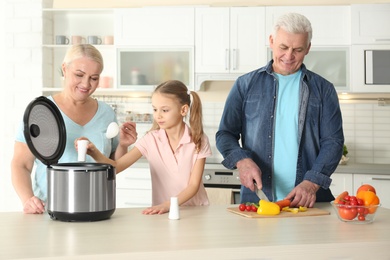 Mature couple and their granddaughter preparing food with modern multi cooker in kitchen