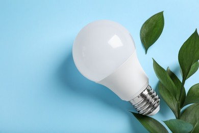 Light bulb and branch with green leaves on color background, flat lay. Space for text