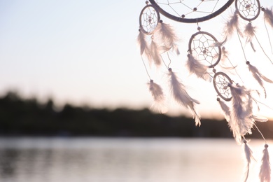 Beautiful handmade dream catcher near river on sunny day. Space for text