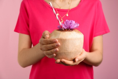Woman holding fresh young coconut with straw on pink background, closeup