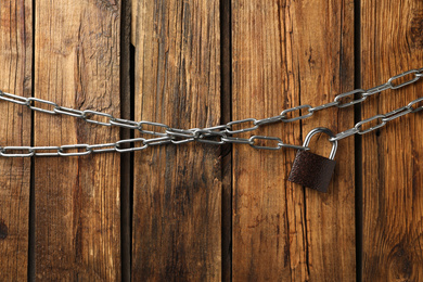 Steel padlock and chains on wooden background, flat lay. Safety concept