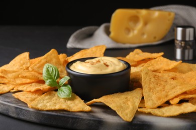Photo of Delicious nachos and cheese sauce with basil on black table