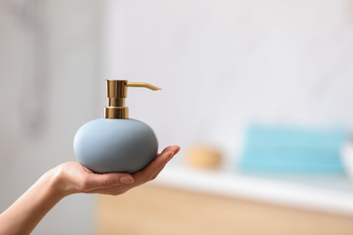 Woman holding soap dispenser on blurred background, closeup. Space for text