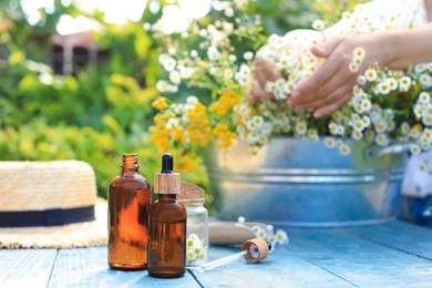 Photo of Woman with flowers near table outdoors, focus on bottles of chamomile essential oil