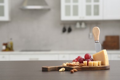 Wooden bord with cut cheese and, nuts and grape on countertop in kitchen, space for text