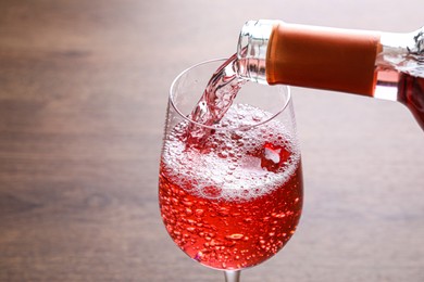 Photo of Pouring delicious rose wine into glass on wooden table, closeup