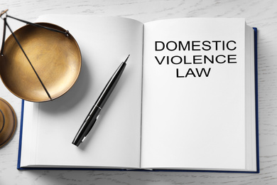 Domestic violence law and scales of justice on white wooden table, above view