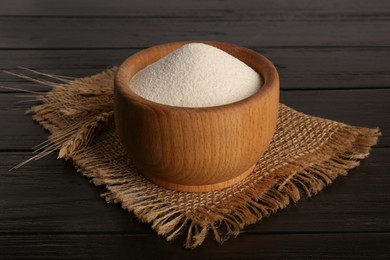 Photo of Fresh semolina in bowl and spikelets on black wooden table