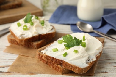 Photo of Bread with cream cheese, green onion and parsley on white wooden table, closeup