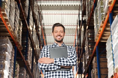 Photo of Happy manager holding clipboard in warehouse with lots of products, low angle view