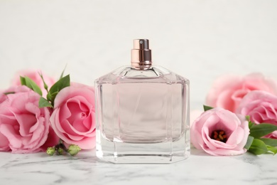Bottle of perfume and beautiful flowers on white marble table